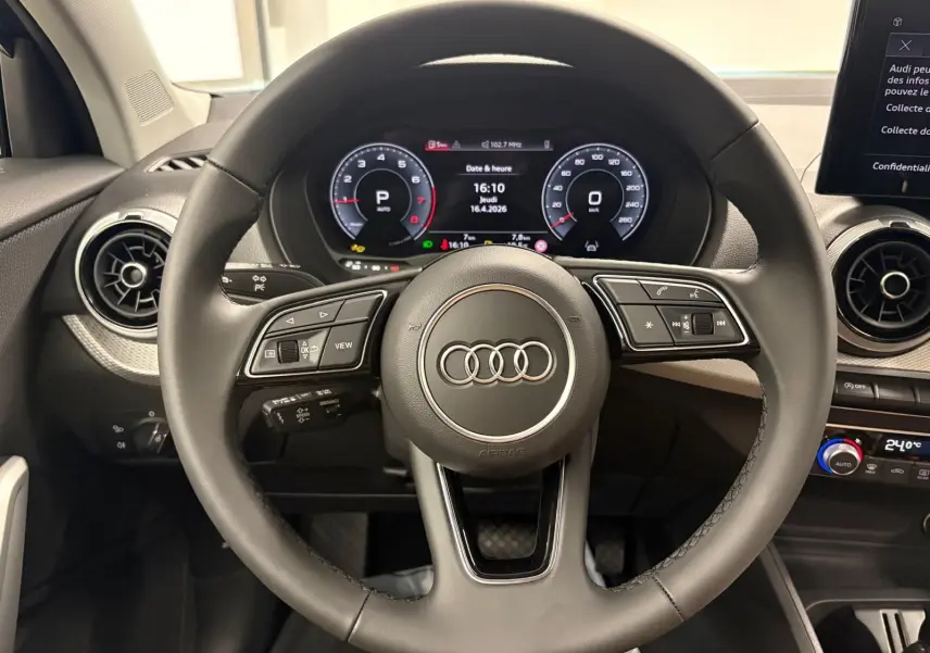 Vue intérieure centrée sur le volant noir de l'Audi Q2 35 TFSI 150 S Line avec tableau de bord numérique allumé.