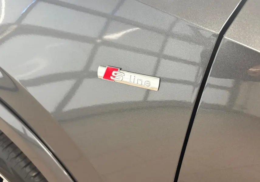 Gros plan sur l'écusson S line sur l'aile avant droite d'un Audi Q2 gris Daytona métallisé.