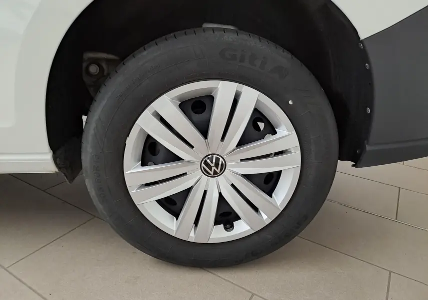 Gros plan sur la roue avant droite du Volkswagen Caddy blanc Candy avec jante acier 16 pouces et enjoliveur argent.