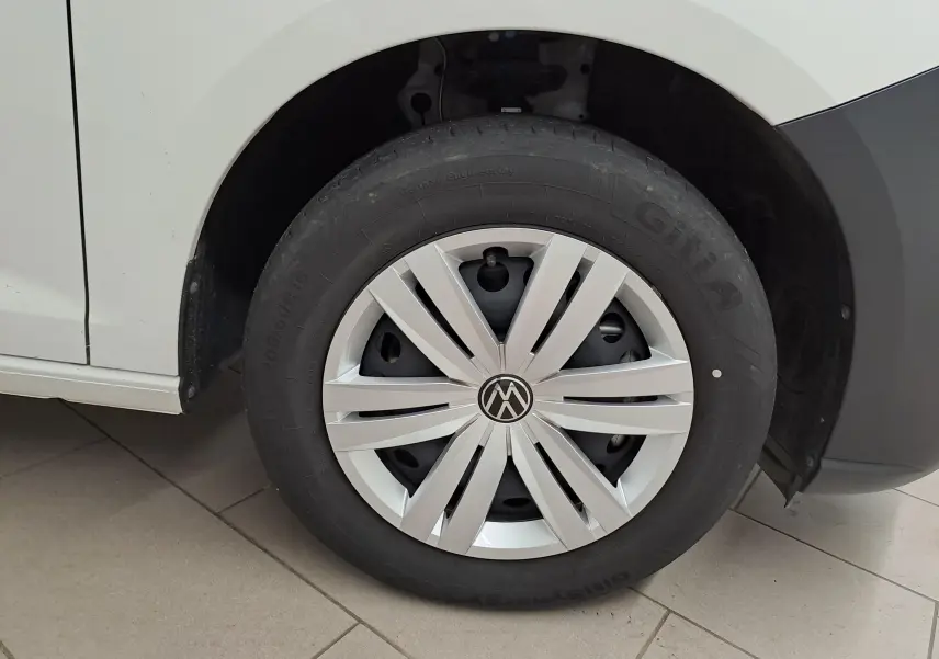 Gros plan sur la roue avant gauche blanche du Volkswagen Caddy 2.0 TDI avec enjoliveur argenté et logo VW central.