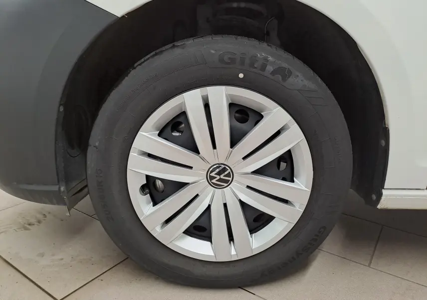 Gros plan sur la roue avant droite d’un Volkswagen Caddy blanc Candy avec jante acier 16 pouces et enjoliveur gris clair.