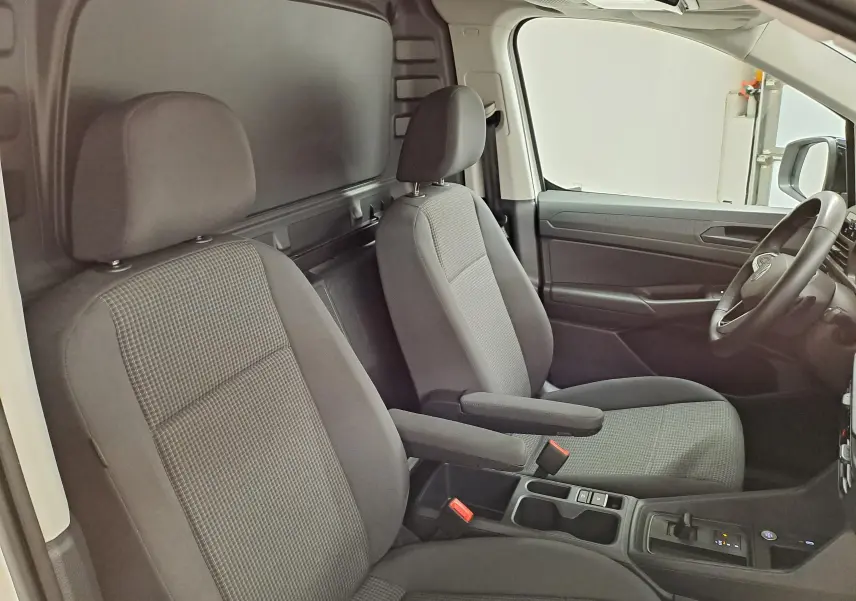 Vue intérieure côté conducteur du Volkswagen Caddy 2025, sièges gris avec accoudoirs et tableau de bord noir.