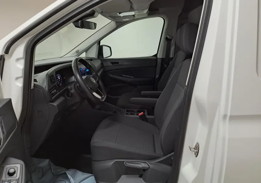 Vue intérieure côté conducteur du Volkswagen Caddy blanc Candy 2025, avec sièges noirs et tableau de bord digital.