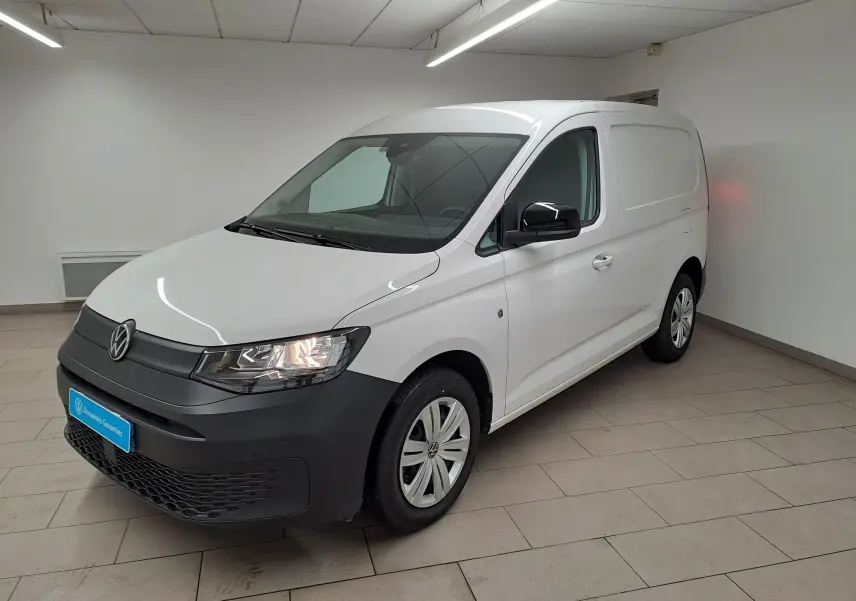 Vue 3/4 avant droit du Volkswagen Caddy blanc Candy avec pare-chocs noir mat et jantes acier 16 pouces en intérieur neutre.