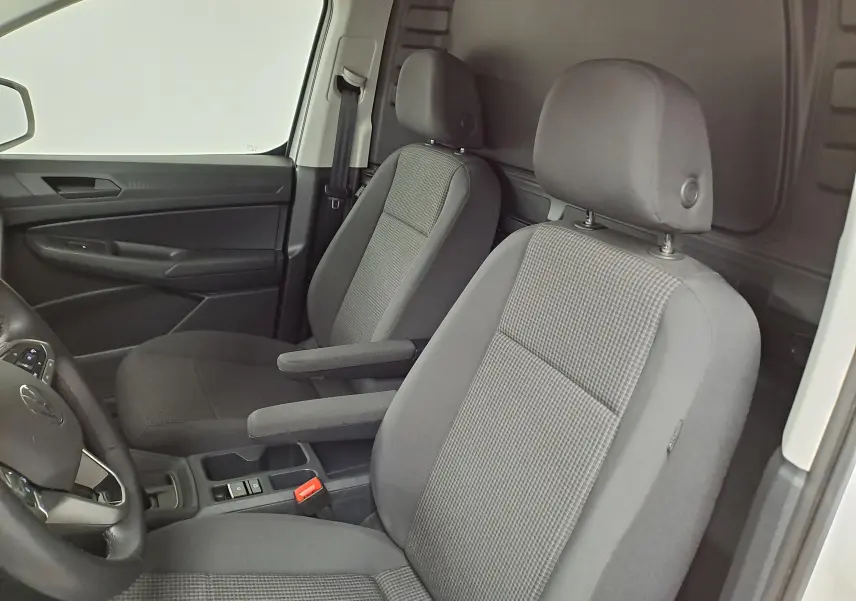 Vue intérieure côté conducteur du Volkswagen Caddy blanc Candy 2025, sièges gris avec accoudoirs et tableau de bord noir.