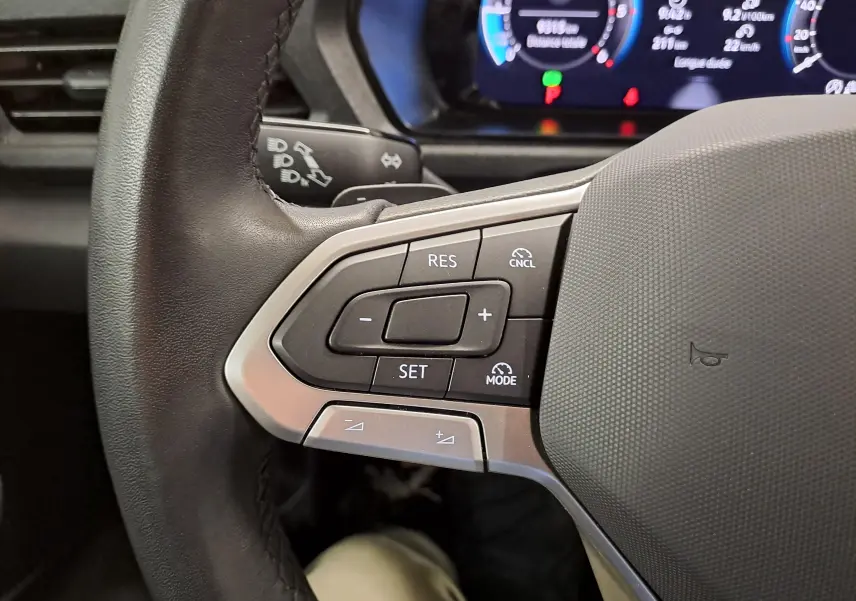 Gros plan sur les commandes de régulateur de vitesse au volant cuir du Volkswagen Caddy 2025, tableau de bord numérique en arrière-plan.