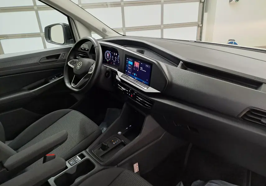 Vue intérieure côté conducteur du Volkswagen Caddy 2025 avec tableau de bord noir et écran tactile central.