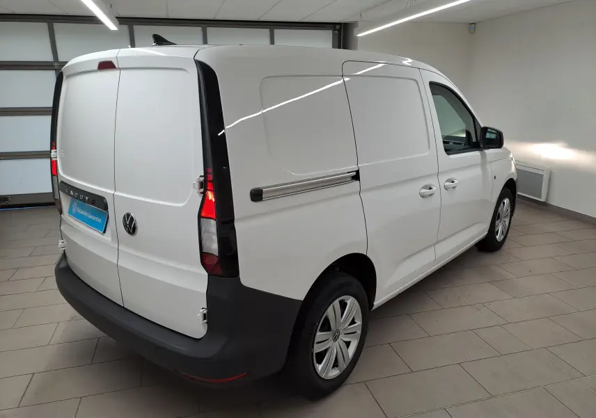 Vue 3/4 arrière droite d'un Volkswagen Caddy blanc Candy avec feux arrière allumés et pare-chocs noir mat.