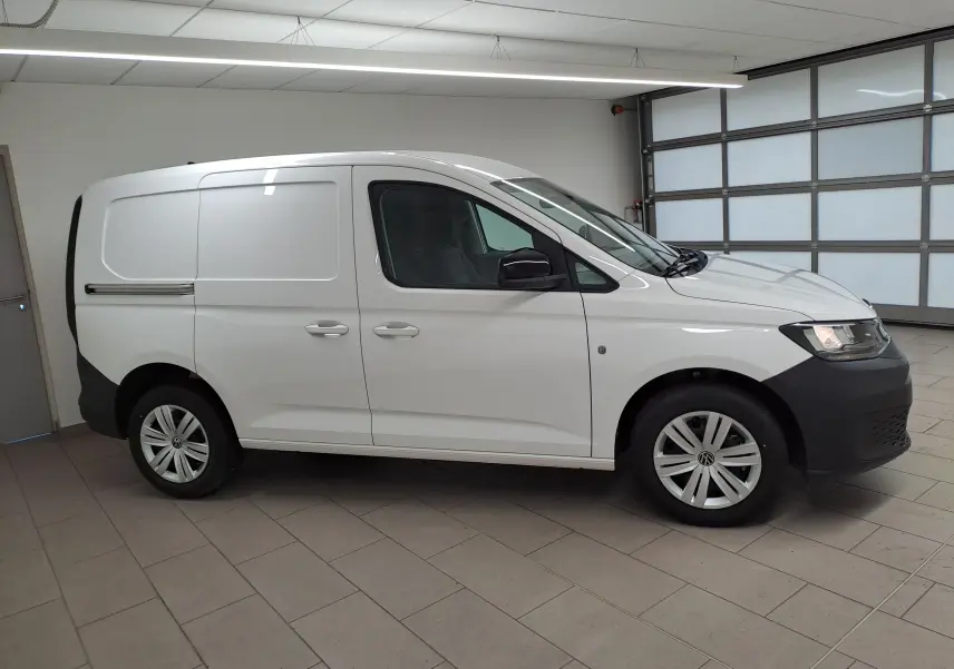 Vue de profil côté gauche d'un Volkswagen Caddy blanc Candy avec rétroviseurs noirs et jantes acier en intérieur lumineux.