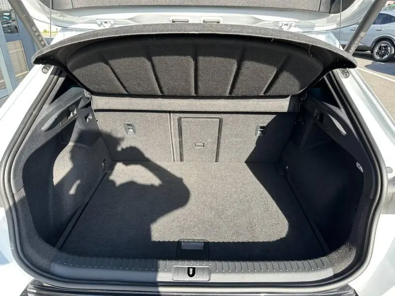 Coffre ouvert vu de l'arrière d'un CUPRA Formentor blanc Nevada métallisé, montrant l'espace de chargement vide et la moquette noire.