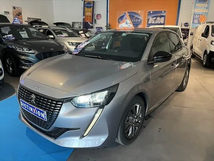 Peugeot 208 gris Artense métal vue 3/4 avant droit en showroom avec phares allumés et calandre distinctive