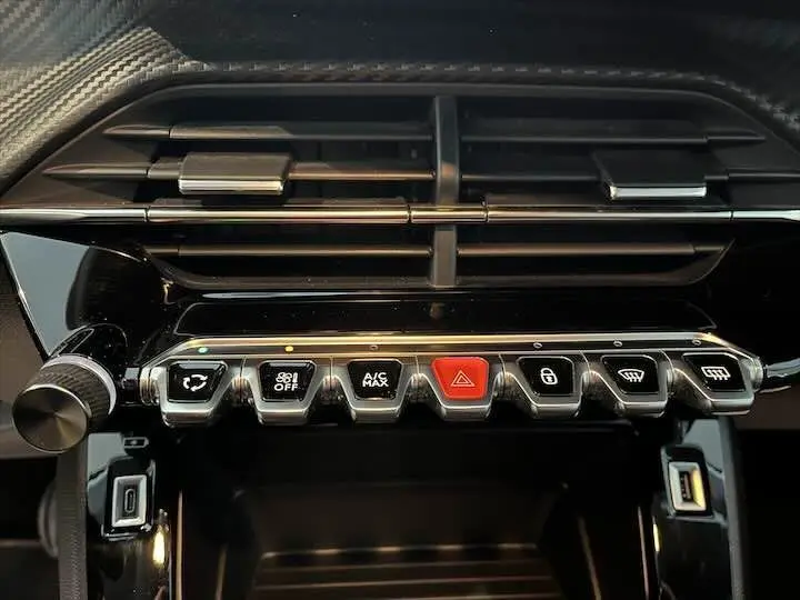 Gros plan sur la console centrale noire brillante de la Peugeot 208 2022, montrant les commandes climatisation et alertes.