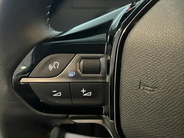 Gros plan sur les commandes de volume et téléphone au volant noir de la Peugeot 208 gris Artense 2022.