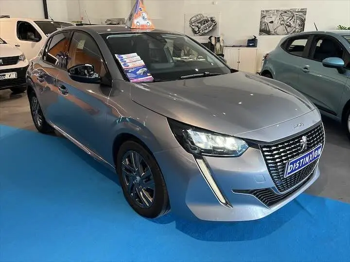 Peugeot 208 gris Artense métal vue 3/4 avant droit en showroom avec phares allumés et plaques Distinxion.