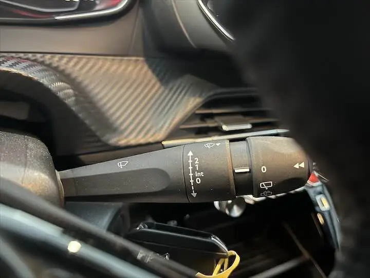 Gros plan sur la commande d'essuie-glace intérieure d'une Peugeot 208 gris Artense métal, tableau de bord noir.