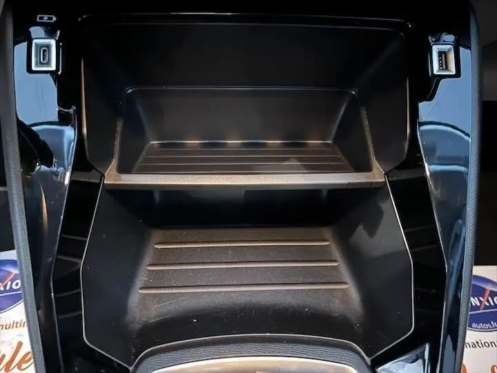 Rangement central noir brillant de la Peugeot 208 1.2 100 CH S&S STYLE, vue en plongée sur l'espace de stockage.