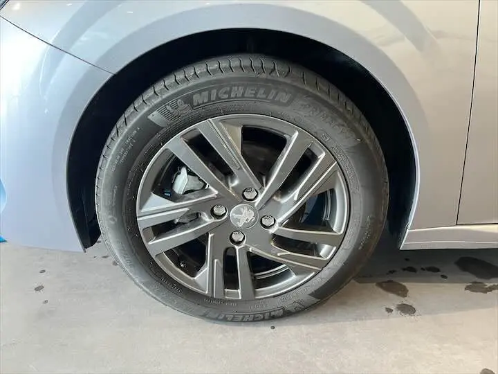 Gros plan sur la roue avant gauche d'une Peugeot 208 gris Artense métal avec jante alliage et pneu Michelin