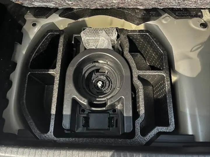 Rangement sous le coffre de la Peugeot 208 gris Artense, vue plongeante sur l'emplacement de la roue de secours.