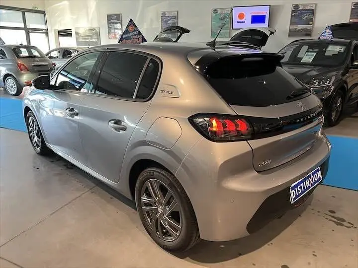 Peugeot 208 gris Artense métal vue 3/4 arrière droit en intérieur avec feux arrière allumés et logo Style sur l'aile.