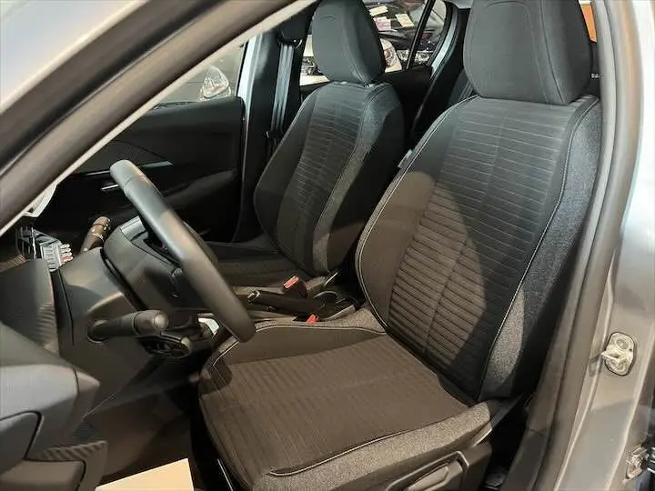 Vue intérieure côté conducteur de la Peugeot 208 gris Artense métal, sièges en tissu gris foncé avec détails texturés.