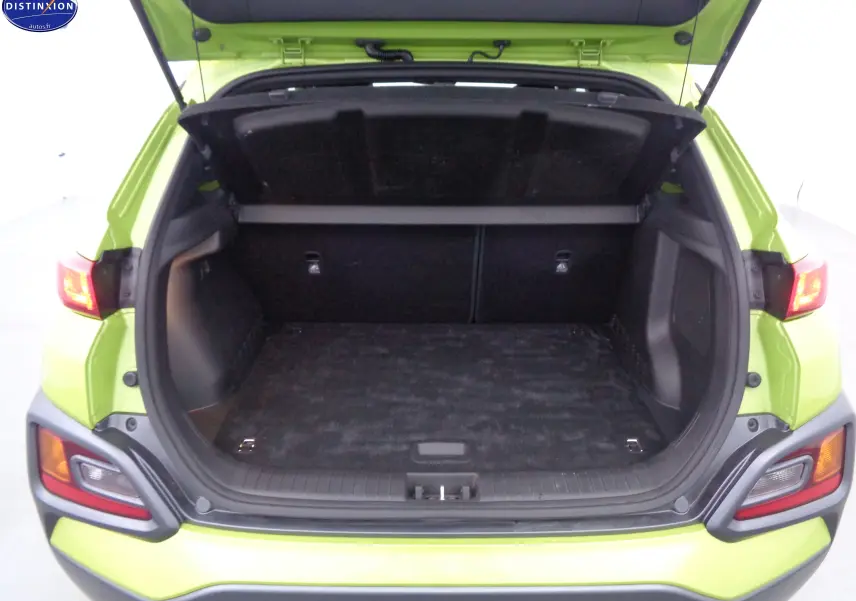 Coffre ouvert vu de l'arrière d'un Hyundai Kona 1.6 CRDI jaune acidulé, montrant l'espace de chargement vide.