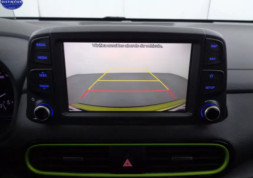 Écran de caméra de recul affichant l'arrière du Hyundai Kona jaune acidulé, avec commandes multimédia autour.