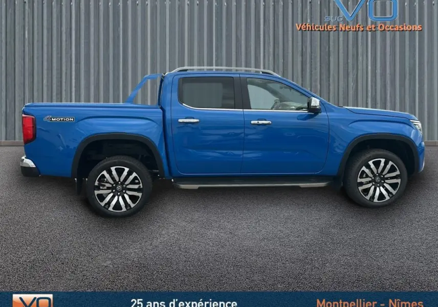 Profil côté gauche du pick-up Volkswagen Amarok bleu 2025 avec jantes alliage 21 pouces et marchepieds visibles.