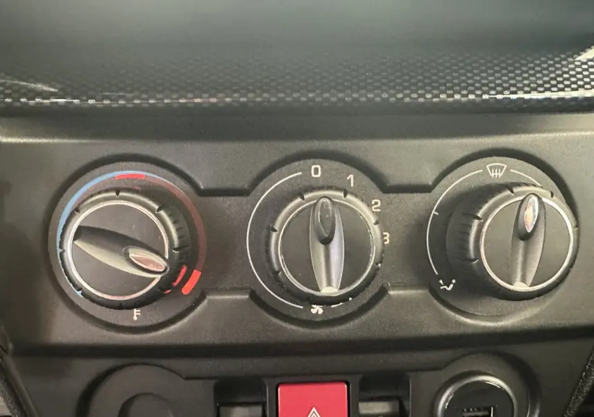 Gros plan sur les commandes de climatisation et bouton de signal d’urgence du tableau de bord d’une Aixam Ambition blanche.