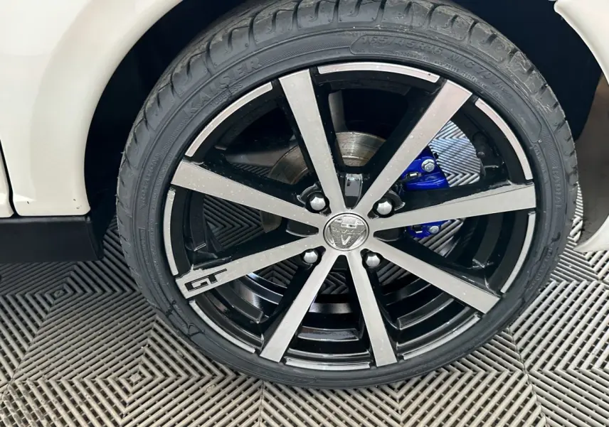 Gros plan sur la roue avant droite de l'AIXAM AMBITION 0.5 CITY GTO blanche avec jante noire et argentée et étrier de frein bleu.