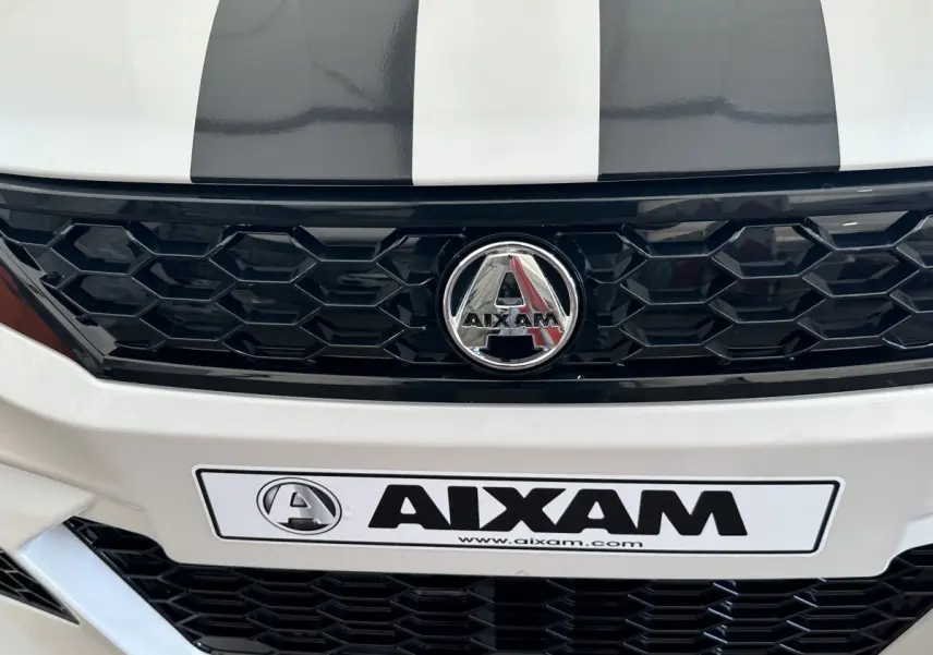 Gros plan avant sur la calandre noire et le logo chromé d'une Aixam Ambition 0.5 City GTO blanche avec bandes grises.