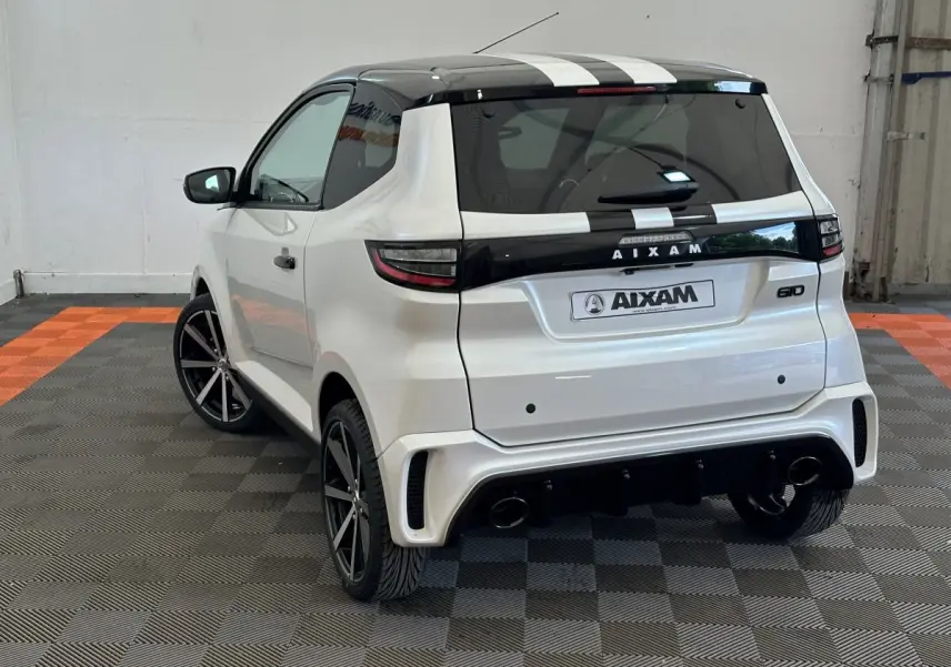 Vue 3/4 arrière droite de l'AIXAM AMBITION 0.5 CITY GTO blanc avec toit noir et bandes blanches, jantes noires, et caméra côté conducteur.