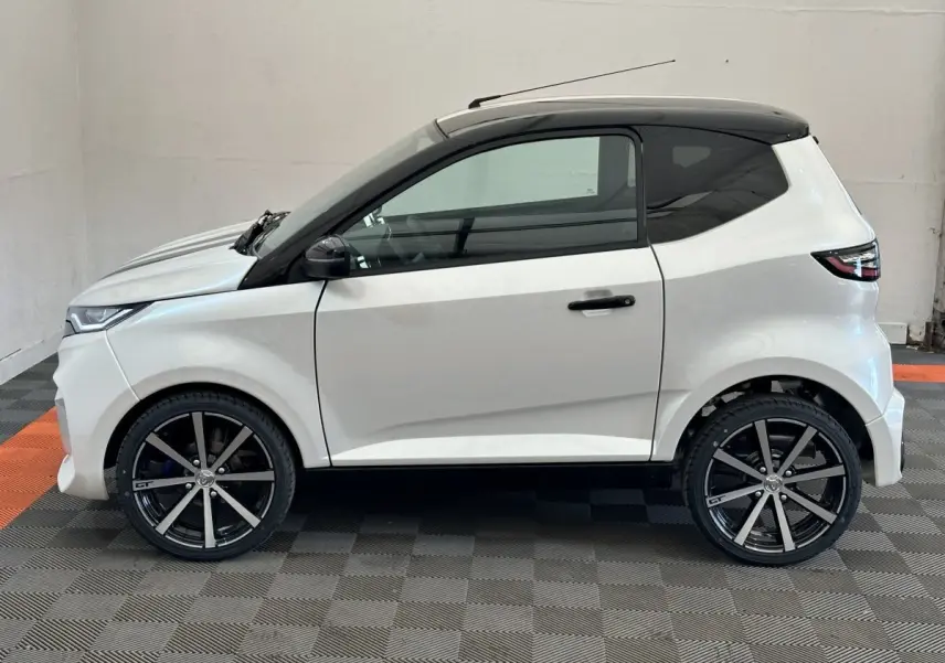 Vue latérale droite d'une Aixam Ambition 0.5 City GTO blanche avec jantes noires et rétroviseur caméra côté conducteur.