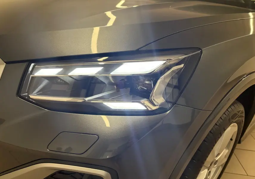 Gros plan sur le phare avant droit allumé de l'Audi Q2 35 TFSI S Line en gris Daytona métallisé.