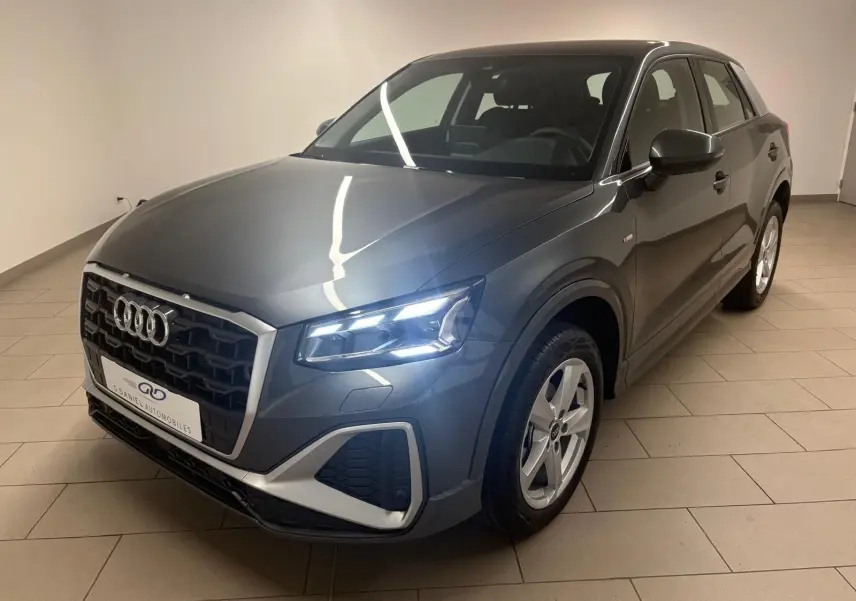 Audi Q2 35 TFSI S Line gris Daytona en 3/4 avant droit, avec phares LED allumés dans un intérieur neutre.