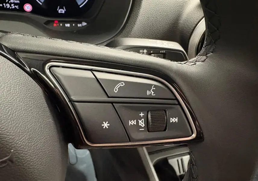 Gros plan sur les commandes du volant de l'Audi Q2 35 TFSI S Line 2026 en Gris Daytona, avec boutons multifonctions visibles.