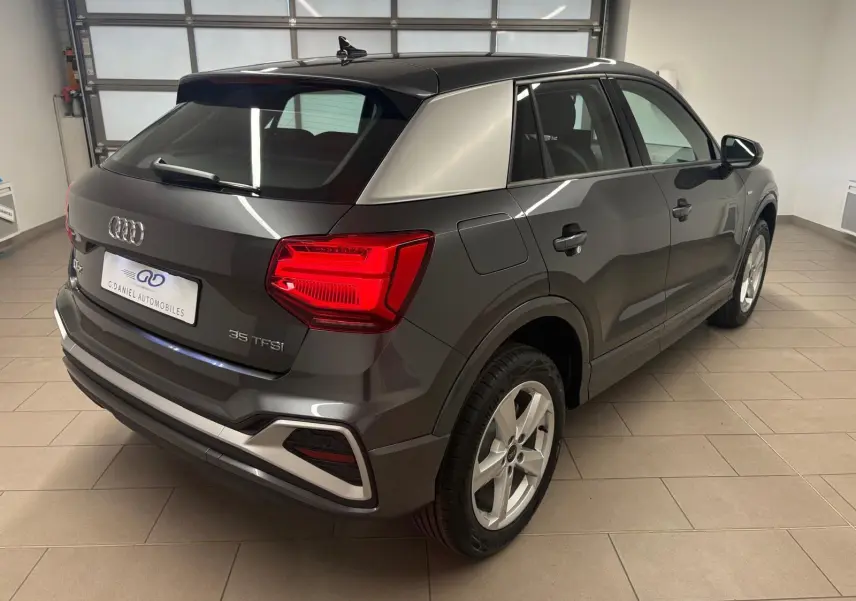 Vue 3/4 arrière droit de l'Audi Q2 35 TFSI S Line 2026 en gris Daytona métallisé dans un garage.