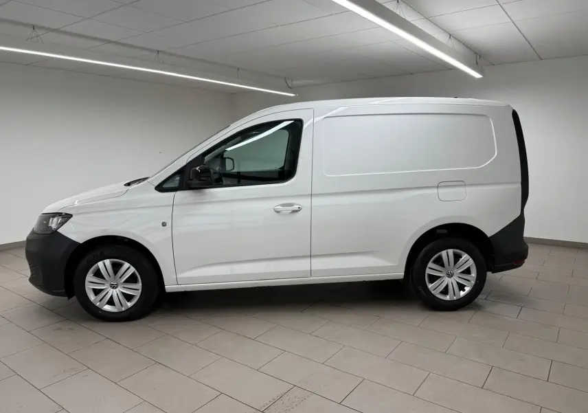 Vue de profil côté gauche d'un Volkswagen Caddy blanc Candy avec pare-chocs et protections noires, en intérieur.