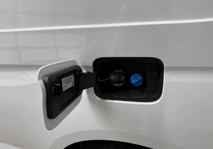 Détail de la trappe à carburant ouverte sur un Volkswagen Caddy blanc candy, avec bouchons diesel et AdBlue visibles.