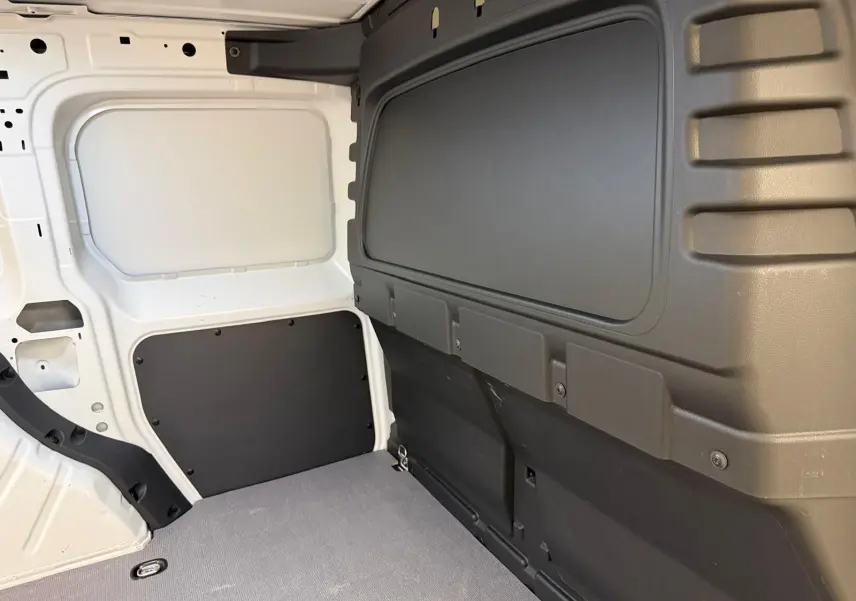 Vue intérieure du compartiment de charge du Volkswagen Caddy blanc Candy, avec parois et plancher protégés en plastique noir.