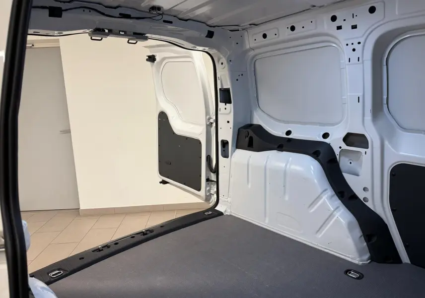 Vue intérieure arrière du Volkswagen Caddy blanc Candy 2025, montrant le compartiment de charge vide et la porte battante ouverte.