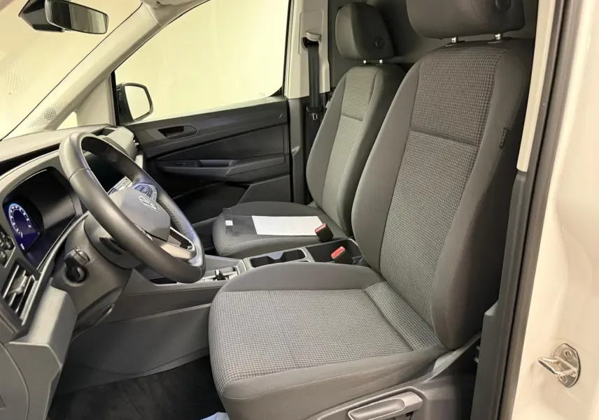 Vue intérieure côté conducteur du Volkswagen Caddy blanc Candy 2025, sièges gris et tableau de bord moderne.