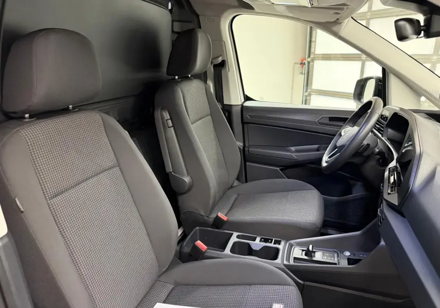 Vue intérieure côté conducteur du Volkswagen Caddy 2025, sièges tissu gris et console centrale avec levier de vitesses.