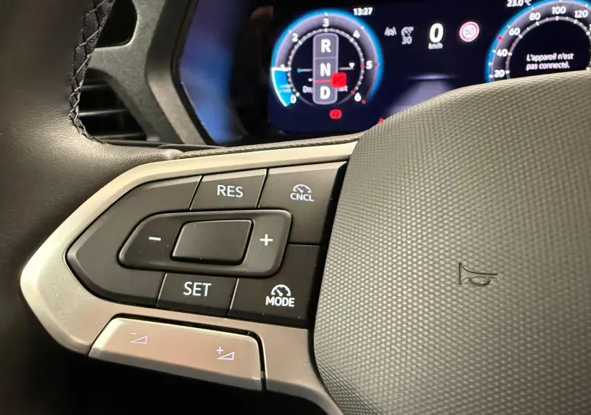 Gros plan sur les commandes au volant à gauche du Volkswagen Caddy blanc 2025 avec affichage numérique en arrière-plan.