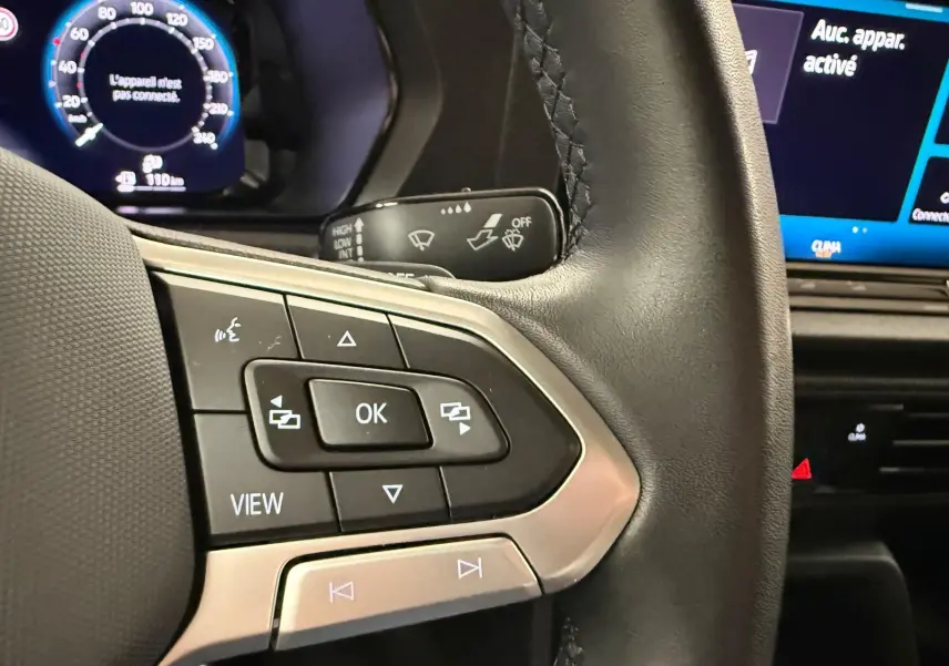 Gros plan sur les commandes multifonctions à gauche du volant cuir du Volkswagen Caddy 2025 avec tableau de bord digital en arrière-plan.