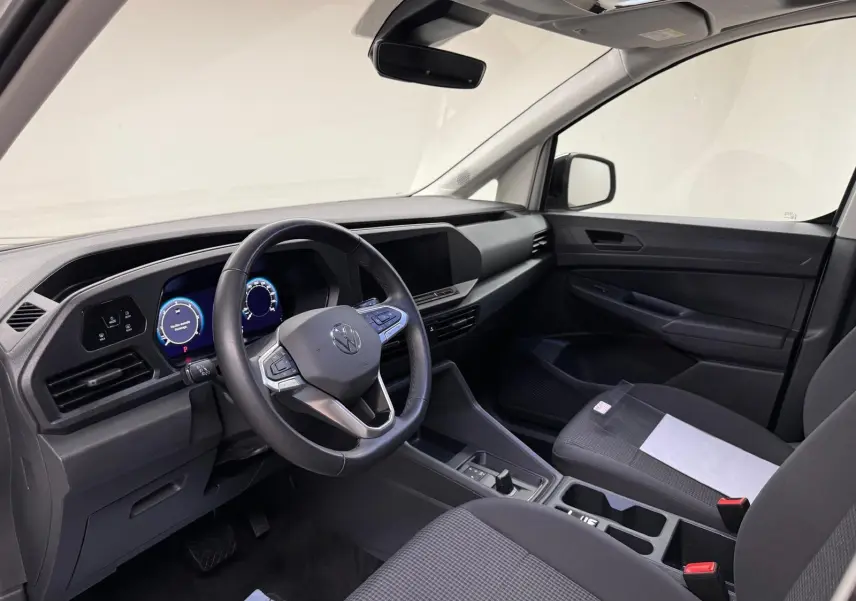 Vue intérieure côté conducteur du Volkswagen Caddy 2025, tableau de bord noir avec volant cuir et écran digital.