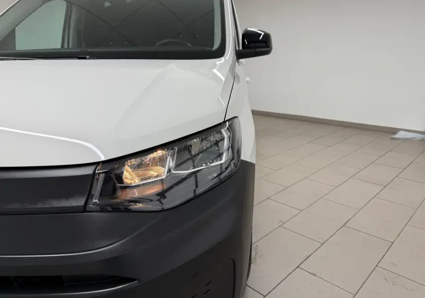 Vue de face droite du Volkswagen Caddy blanc Candy avec phare avant allumé et pare-chocs noir mat.