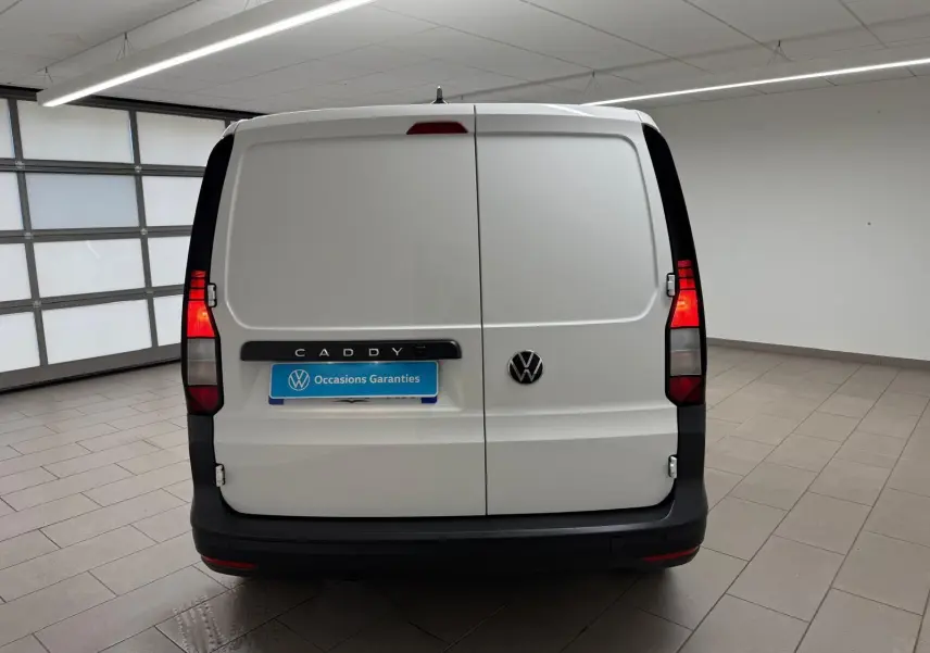 Vue arrière d'un Volkswagen Caddy blanc Candy avec portes battantes et feux arrière allumés en intérieur.