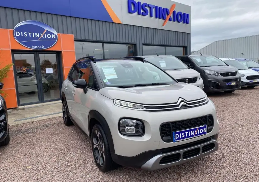 Citroën C3 Aircross grise vue 3/4 avant avec toit noir et détails noirs autour des phares, devant un concessionnaire.
