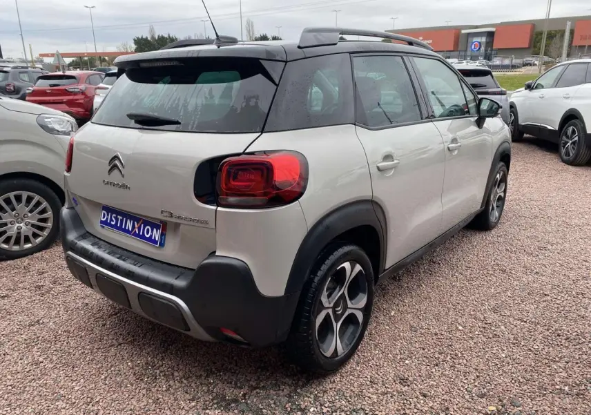 Vue 3/4 arrière droite d’un Citroën C3 Aircross gris 2020 avec toit noir et jantes distinctives, stationné sur un sol gravillonné.