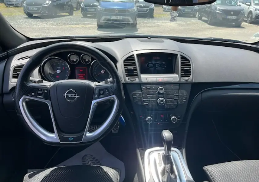Vue intérieure centrée sur le tableau de bord et volant d’une Opel Insignia Sports Tourer gris clair, avec console centrale et levier de vitesse automatique.